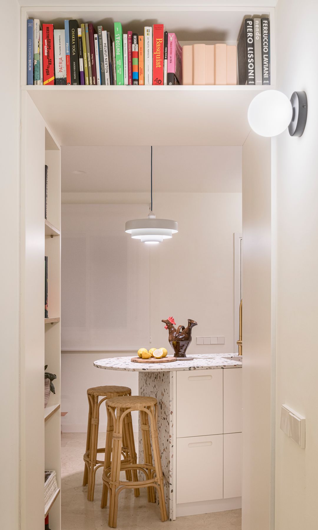 Estantería sobre puerta de paso con libros, acceso cocina, isla de cocina, taburetes de madera