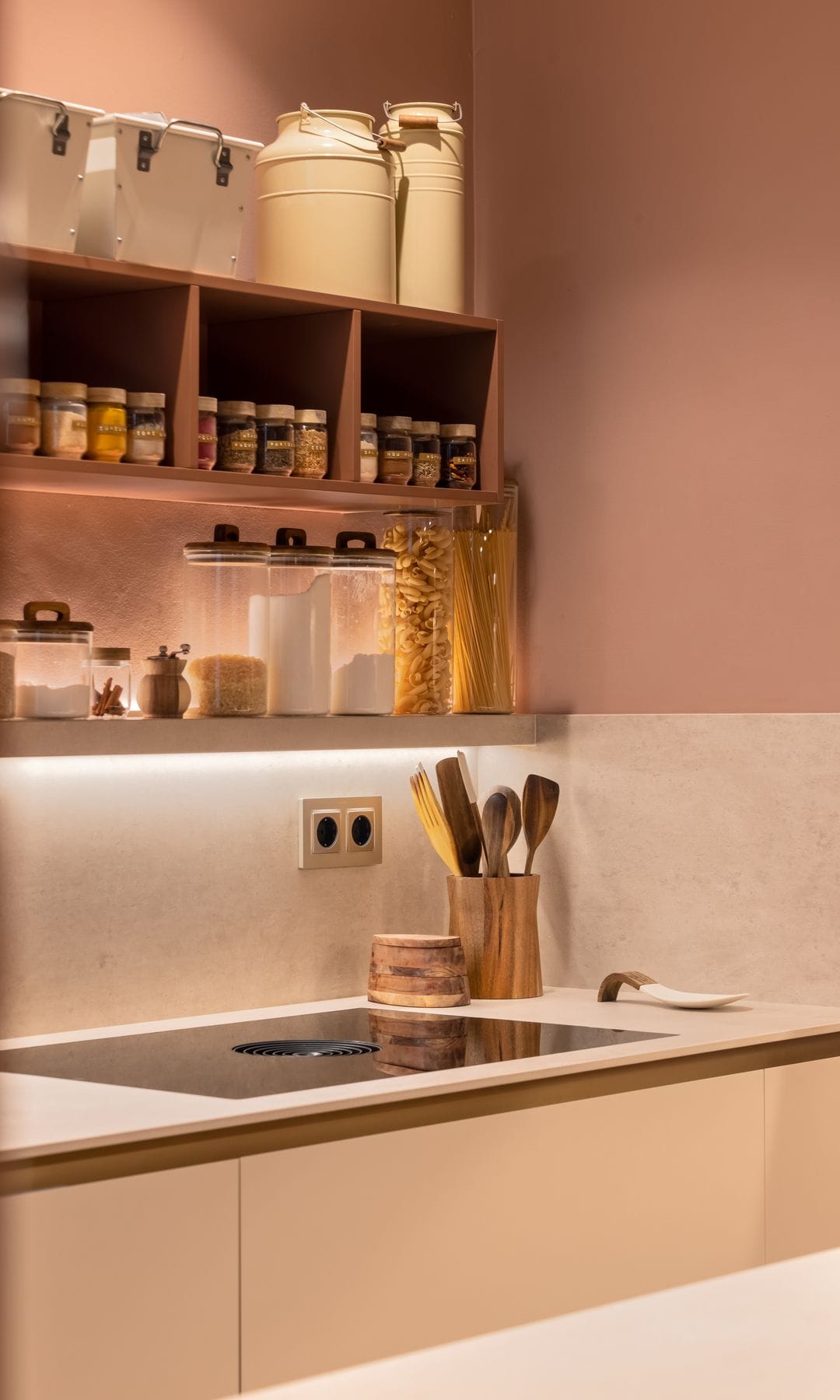 Cocina en tonos beiges con iluminación bajo los armarios superiores, botes de cristal para las especies y la pasta, accesorio para los utensilios de cocina, cajas 