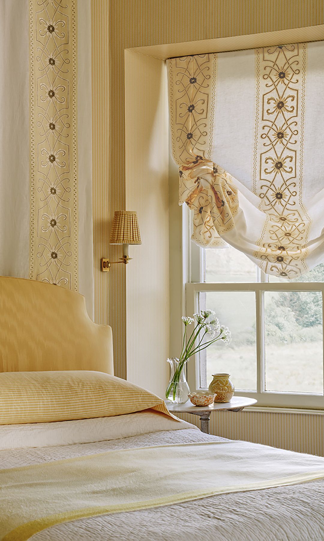 Dormitorio con cabecero tapizado amarillo, estor amarillo con cena vertical, ropa de cama amarilla y blanca, aplique de pared
