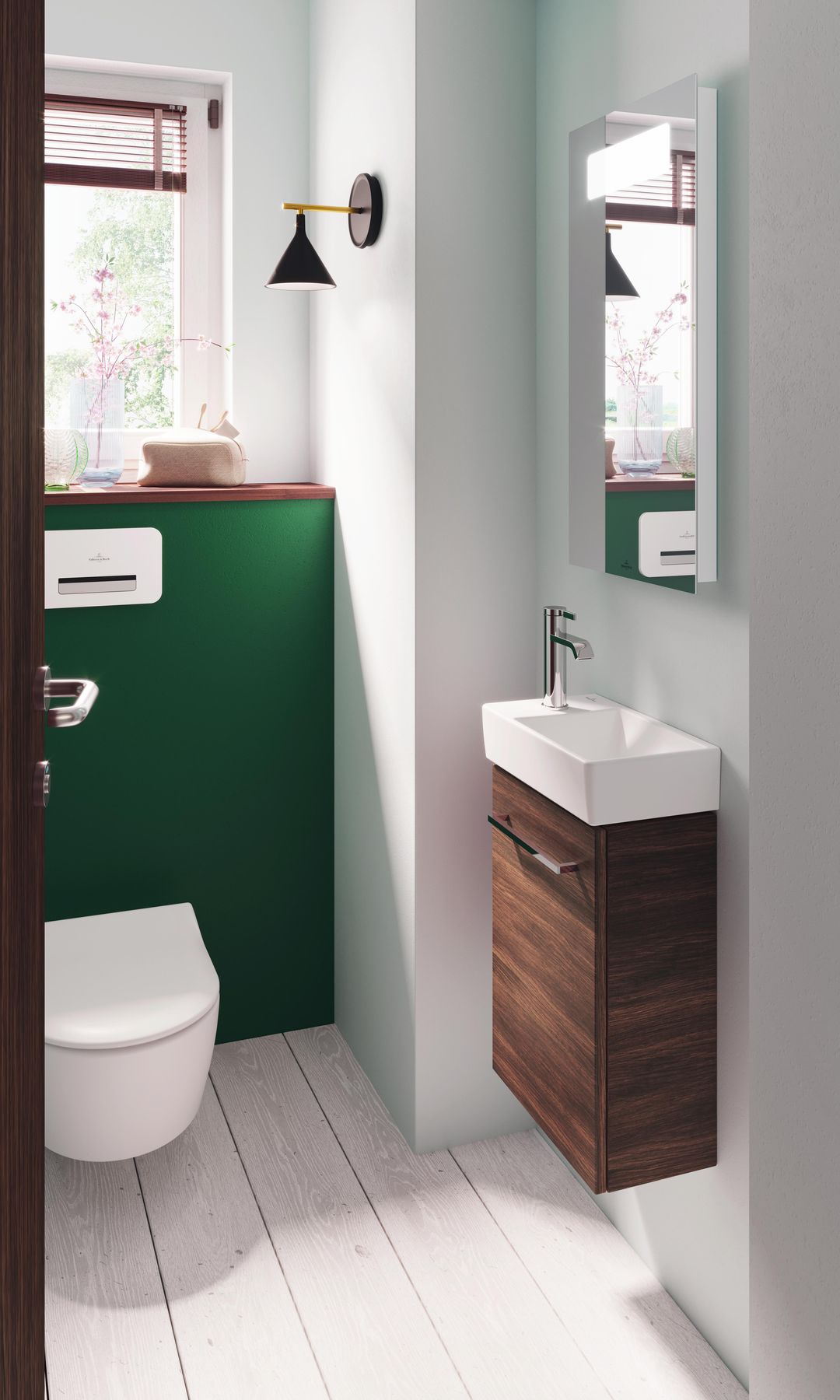 Baño pequeño con ventana, pared de color verde oscura, lavabo y mueble pequeño, espejo, sanitario suspendido