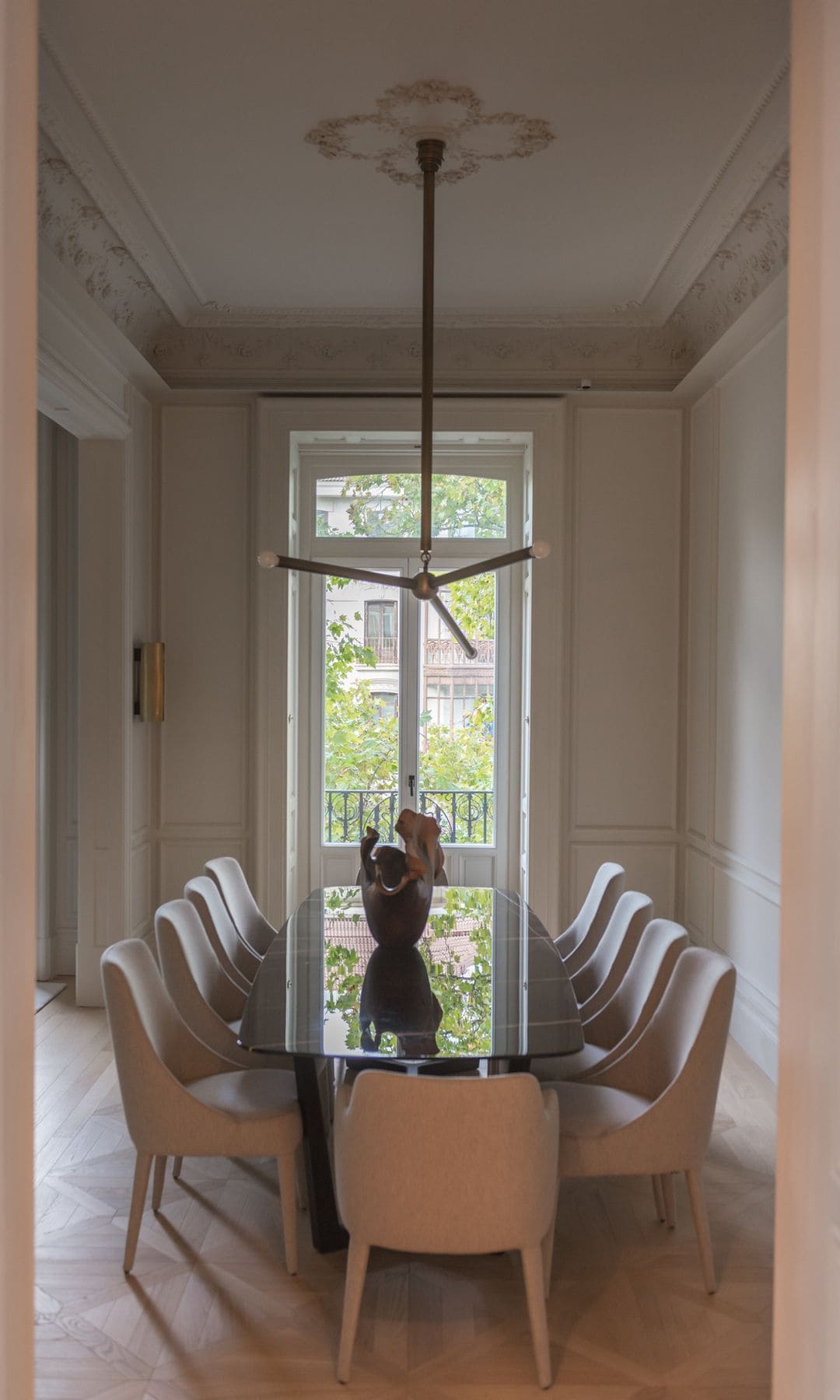 Comedor con mesa ovalada, sillas tapizadas, lámpara de techo, ventana y techo con molduras