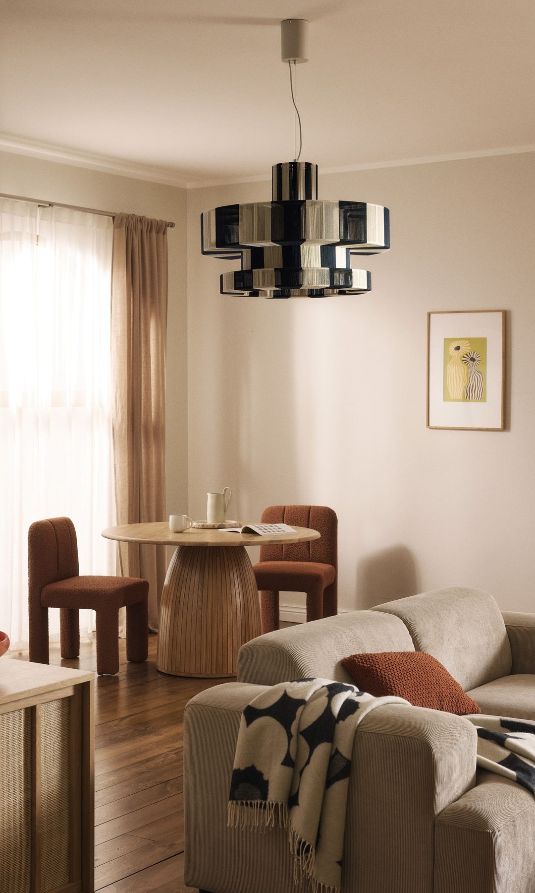 Salón comedor, con lámpara de techo metalizada, mesa de comedor redonda, sofá beige, manta de cuadros, suelo de madera