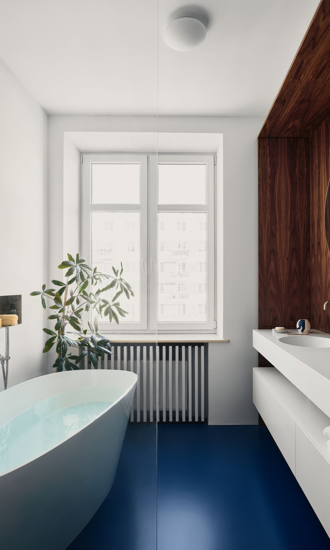 Baño con el suelo azul, bañera exenta, pared de madera, cubrerradiador, encimera y mueble bajolavabo blancos