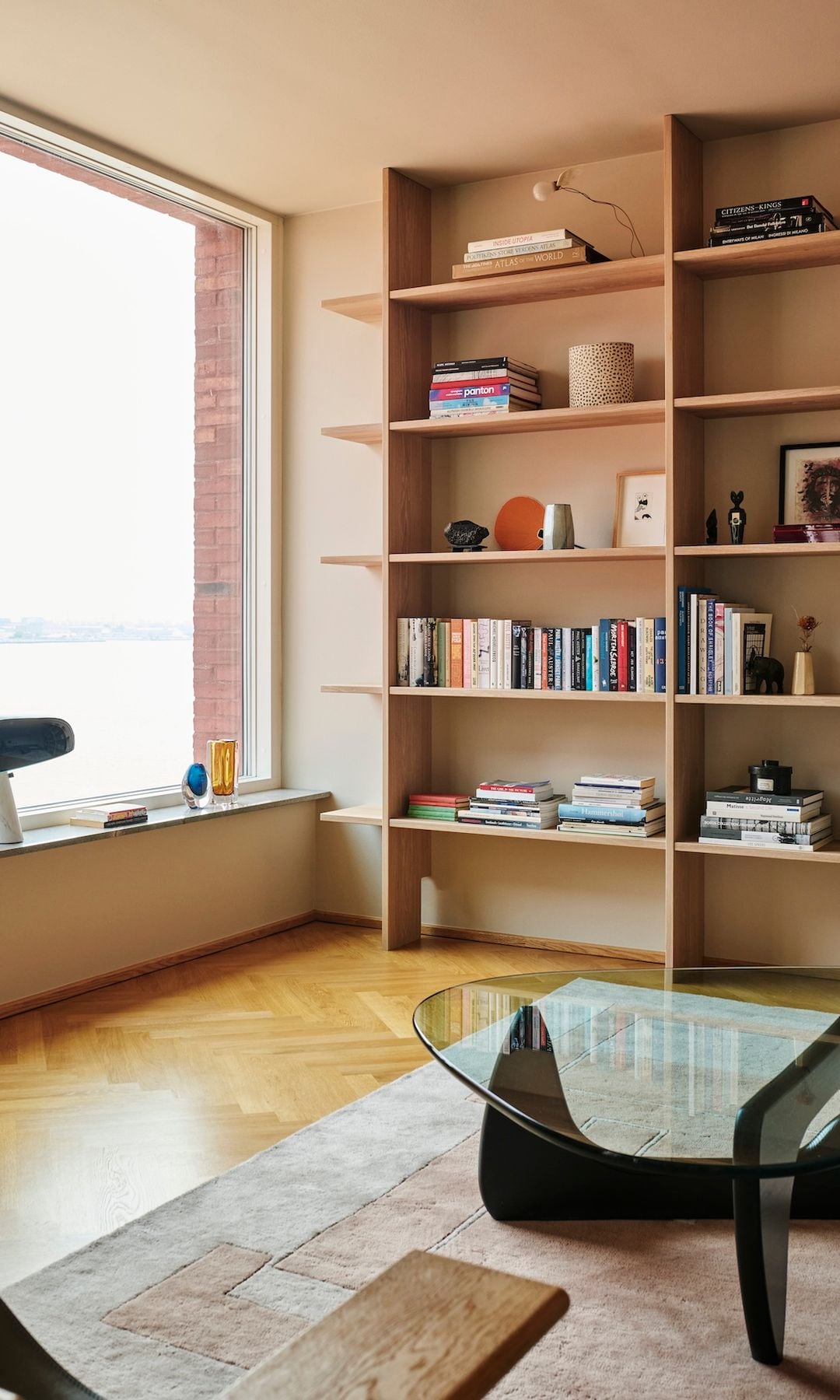 Salón con mesa de centro tipo Isamy Noguchi, librería de madera si. trasera, gran ventanal, banco bajo la ventana, alfombra