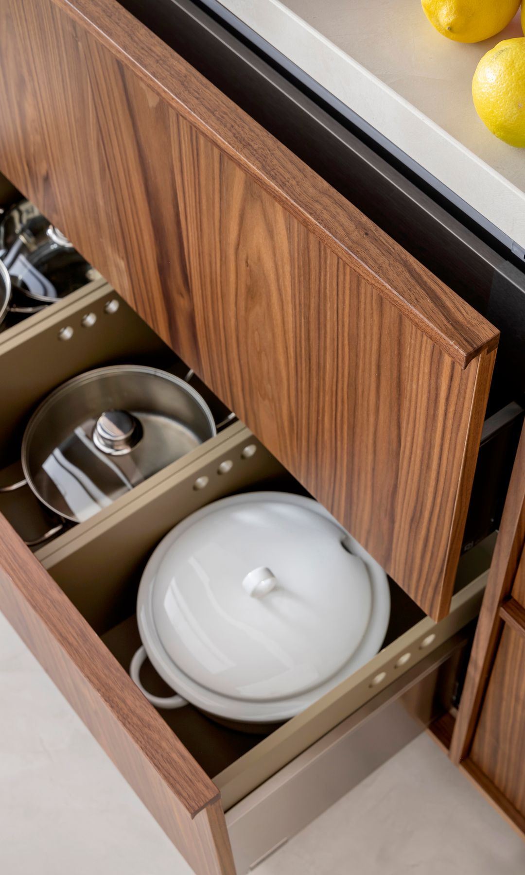 Gaveta de cocina abierta con cacerolas, mueble de madera oscura y encimera blanca 