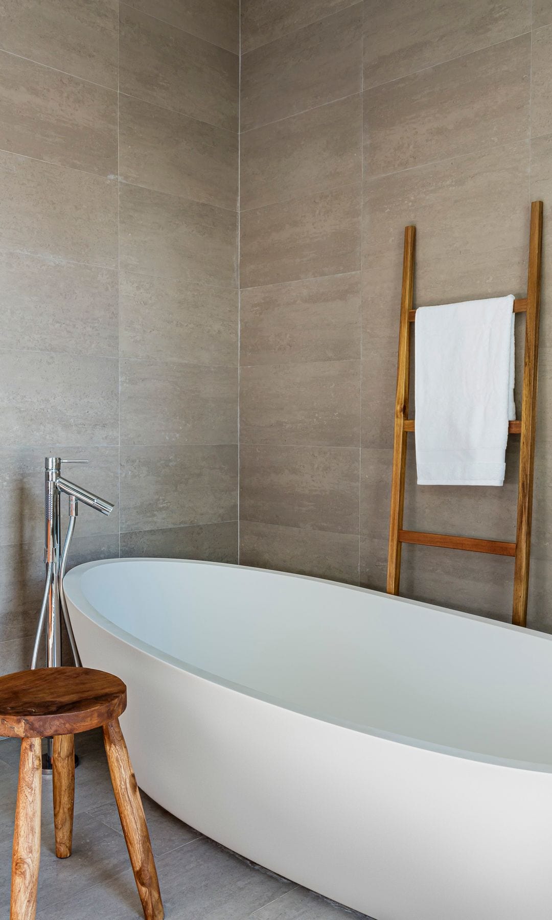 Baño con bañera exenta, grifería de suelo, taburete de madera, escalera de madera a modo toallero