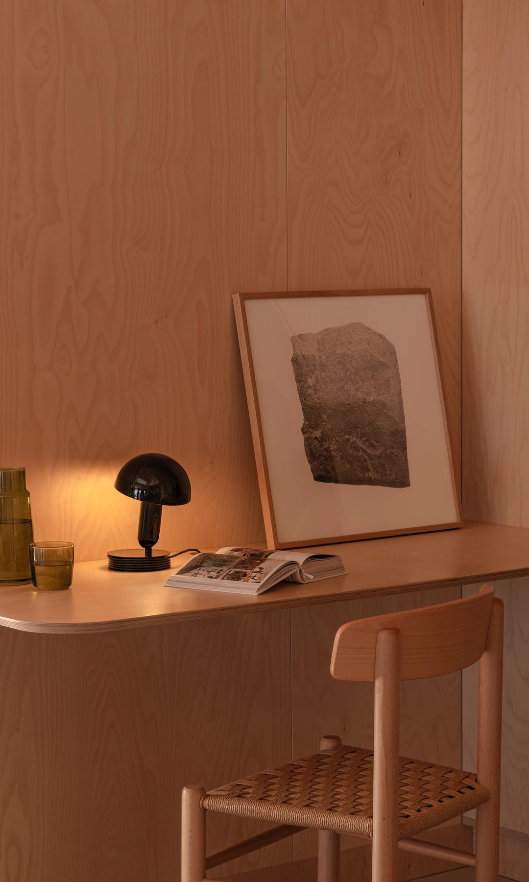 Mesa de escritorio con silla de enea, cuadro, jarra con vaso de agua y lámpara negra de sobremesa 