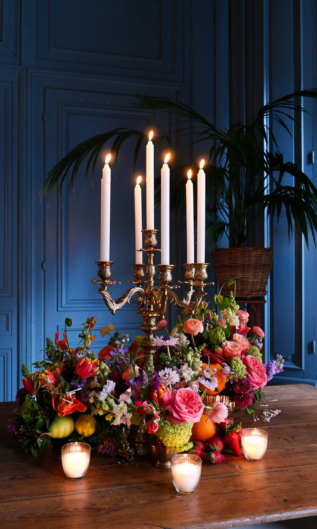 Mesa de comedor de madera, candelabro XL dorado, velas y varios centros de flores, paredes con molduras azules 