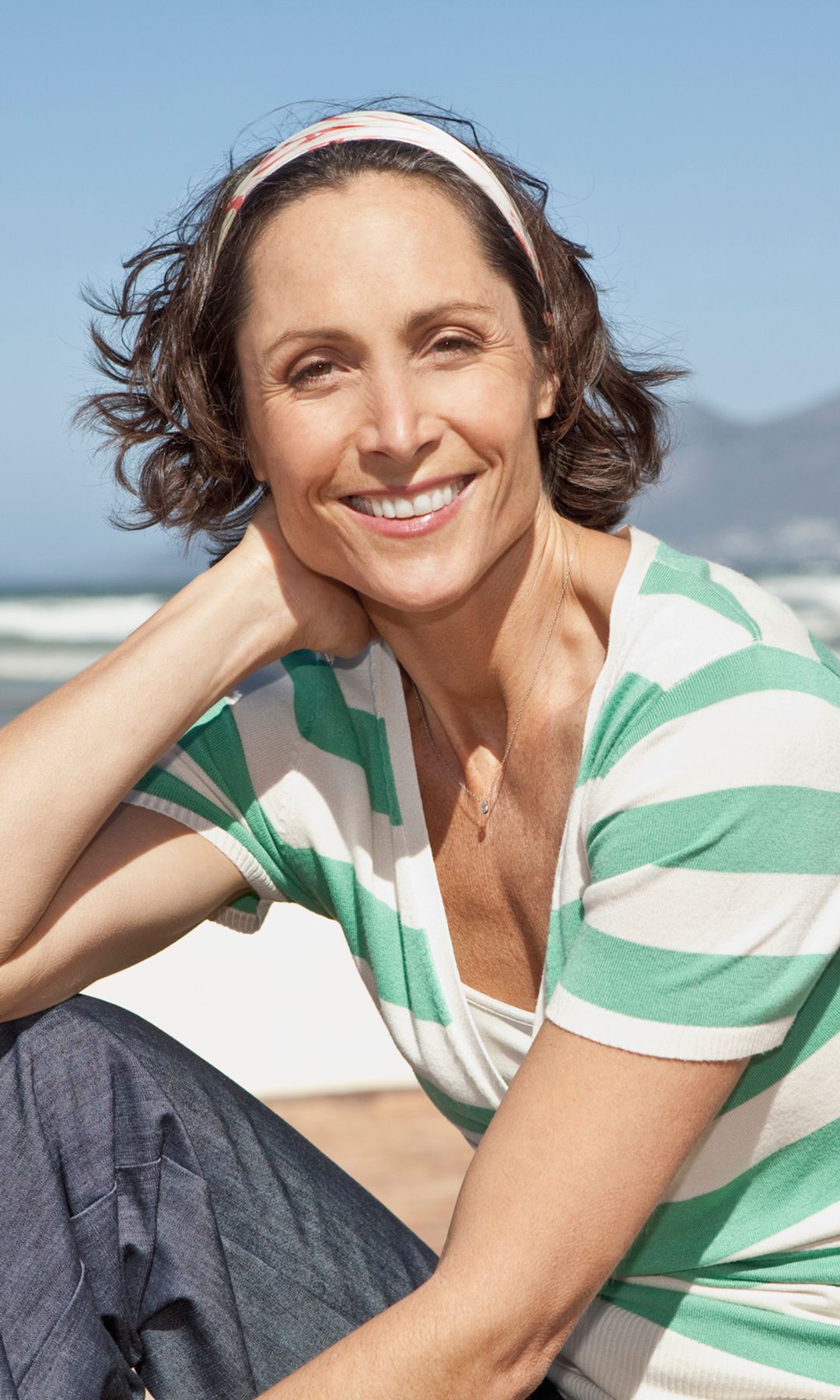 Mujer de 50 en la playa mirando a cámara feliz