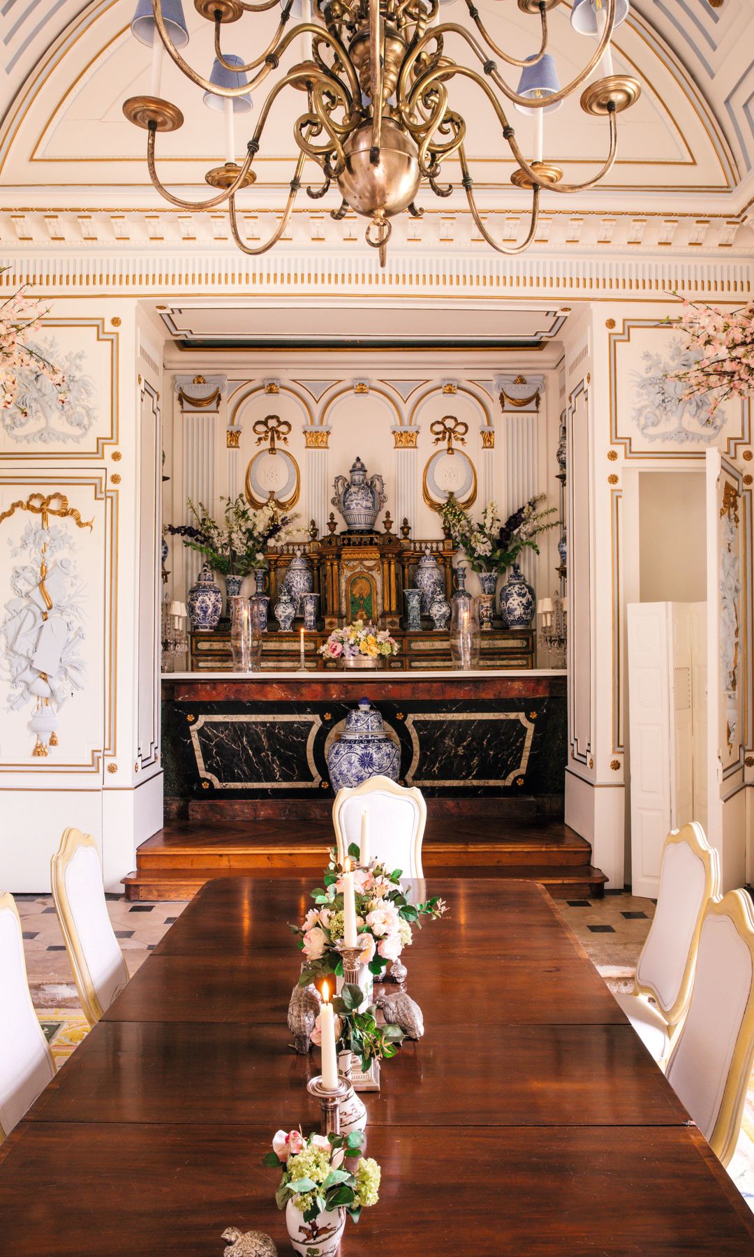 Comedor lujoso con mesa larga, sillas blancas, candelabro, y flores