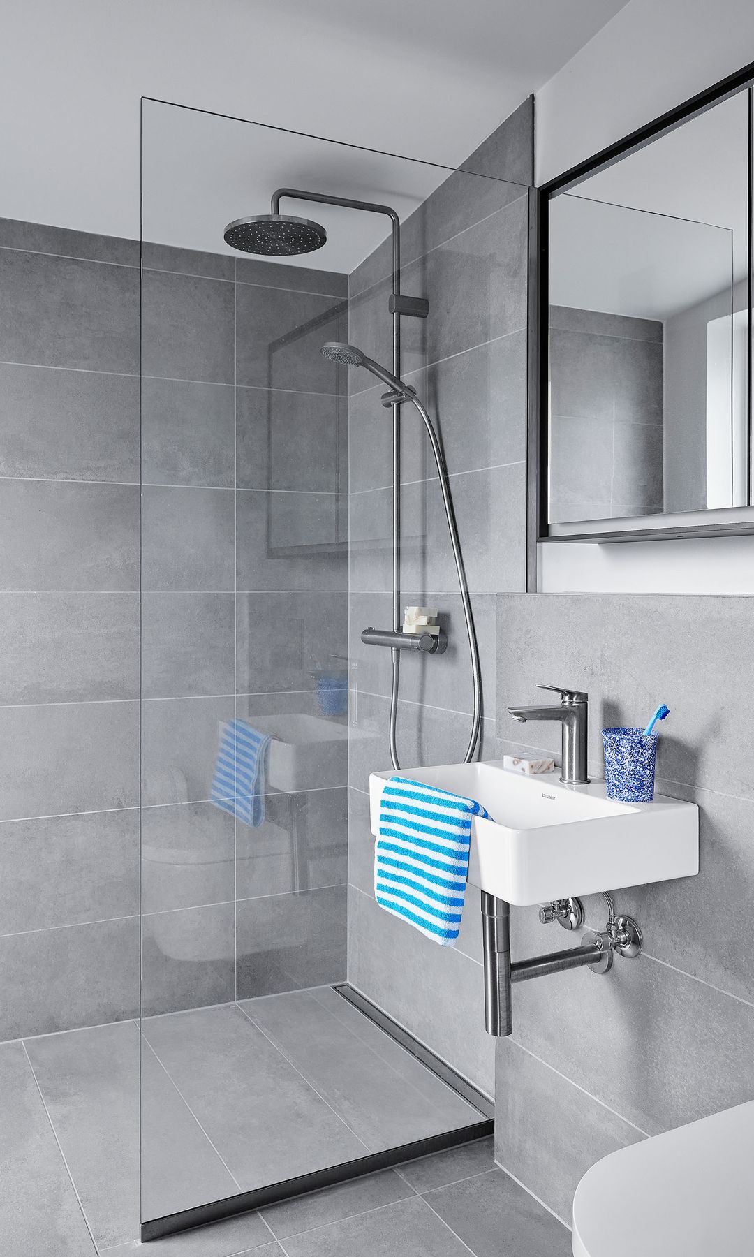 Baño pequeño con ducha, azulejos grises en suelo y paredes, mampara, lavabo suspendido