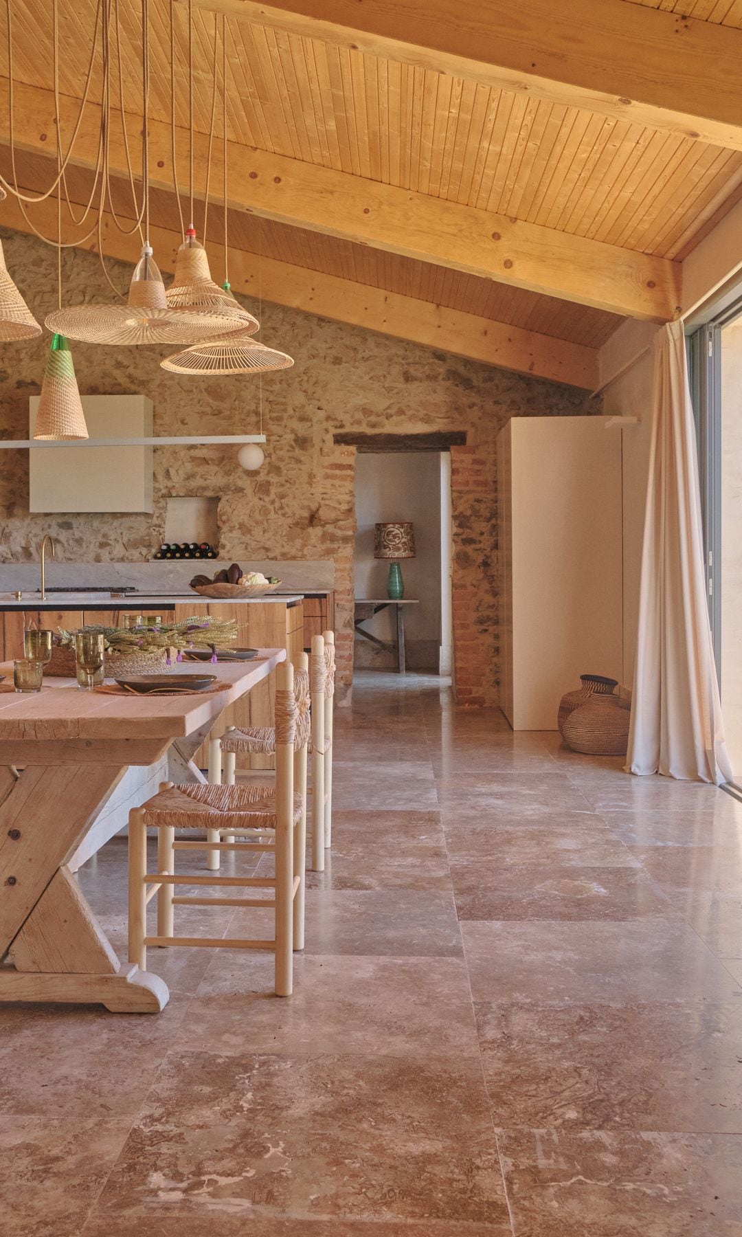 Cocina con suelo de piedra natural, techo de madera, isla y mesa de madera adosada, lámpara de techo 