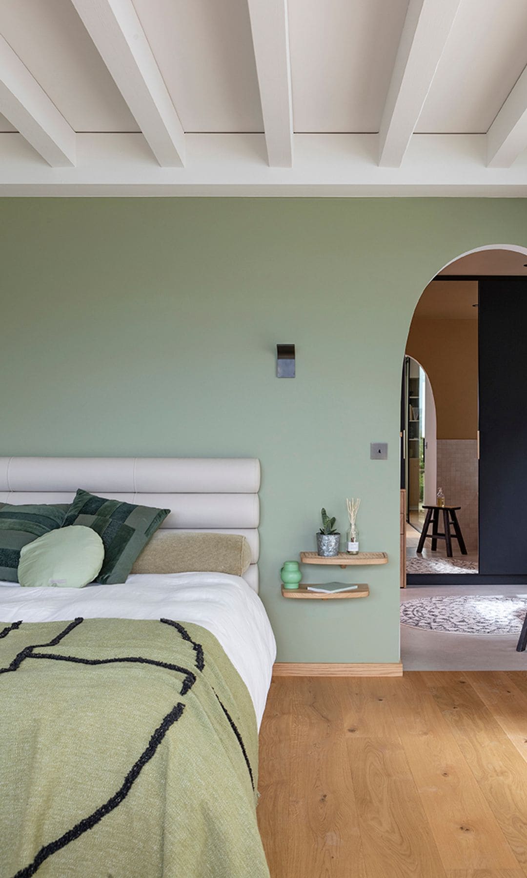 Dormitorio con vigas blancas en el techo, paredes verde menta, cabecero tapizado blanco, ropa de cama verde, cojines verdes, suelo de madera