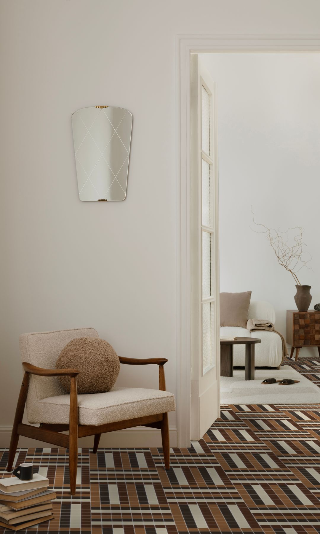 Rincón de lectura con suelo porcelánico con baldosas con formas geométricas en colores marrón, blanco y negro, butaca tapizada y libros en el suelo