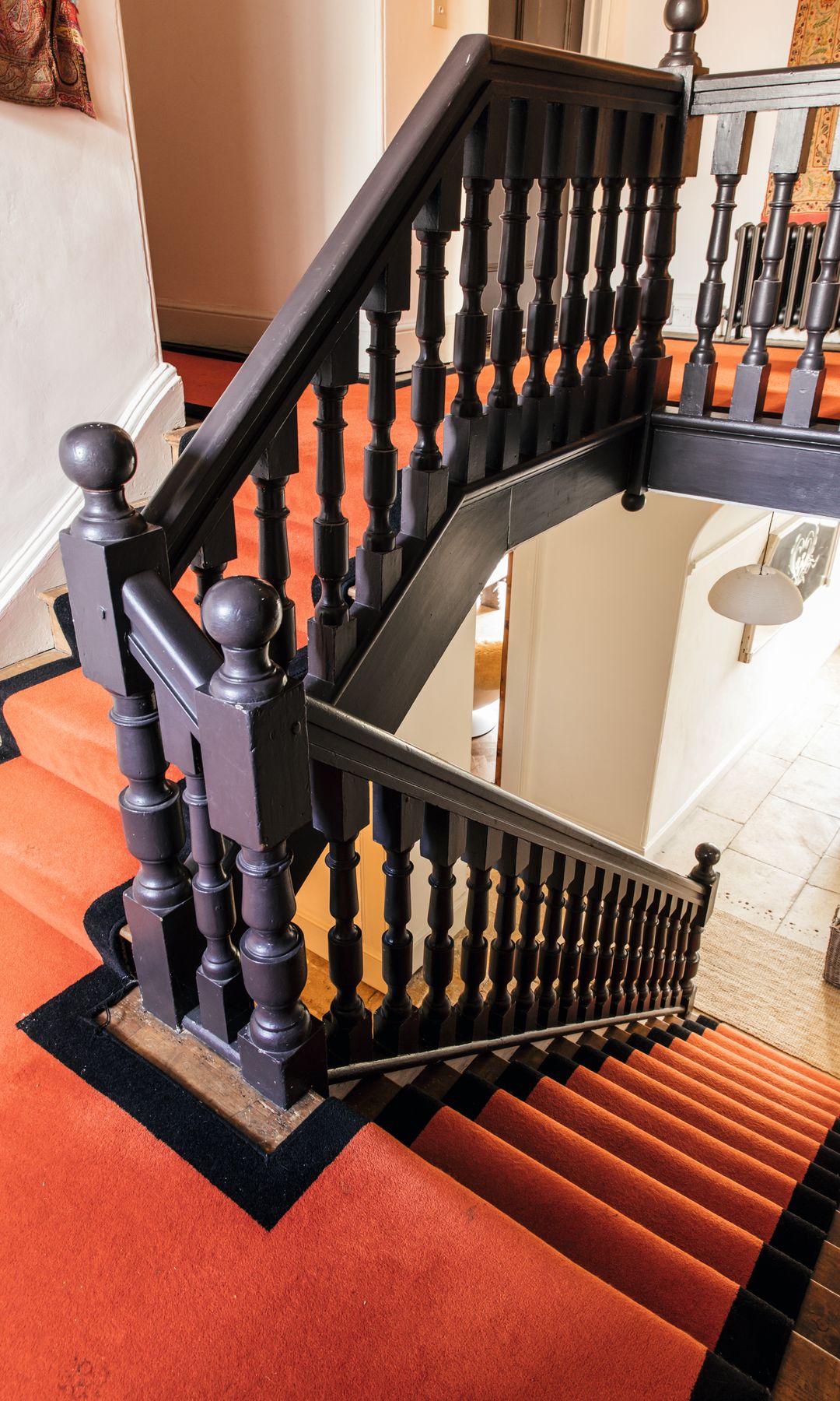 Escalera de madera con barandilla negra y alfombra naranja y negra.
