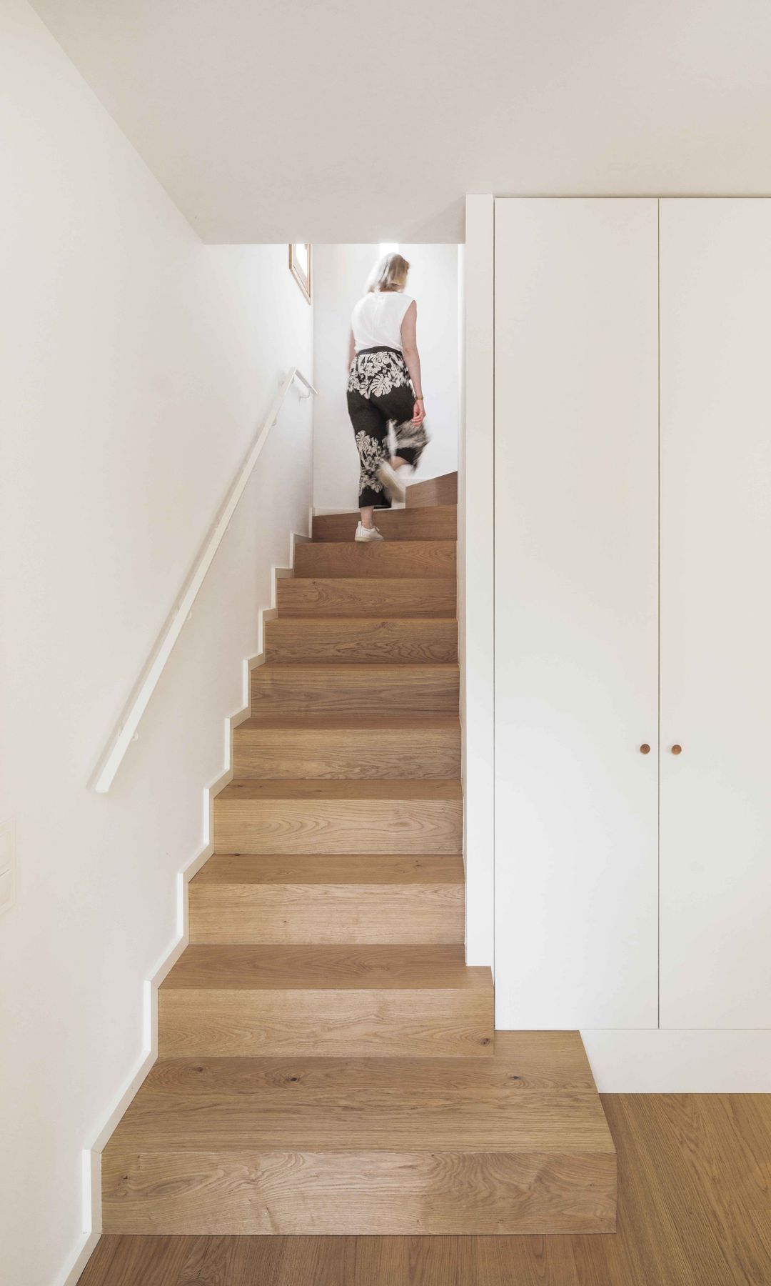 Mujer subiendo escalera de madera, entrada con armario blanco y hornacina de madera