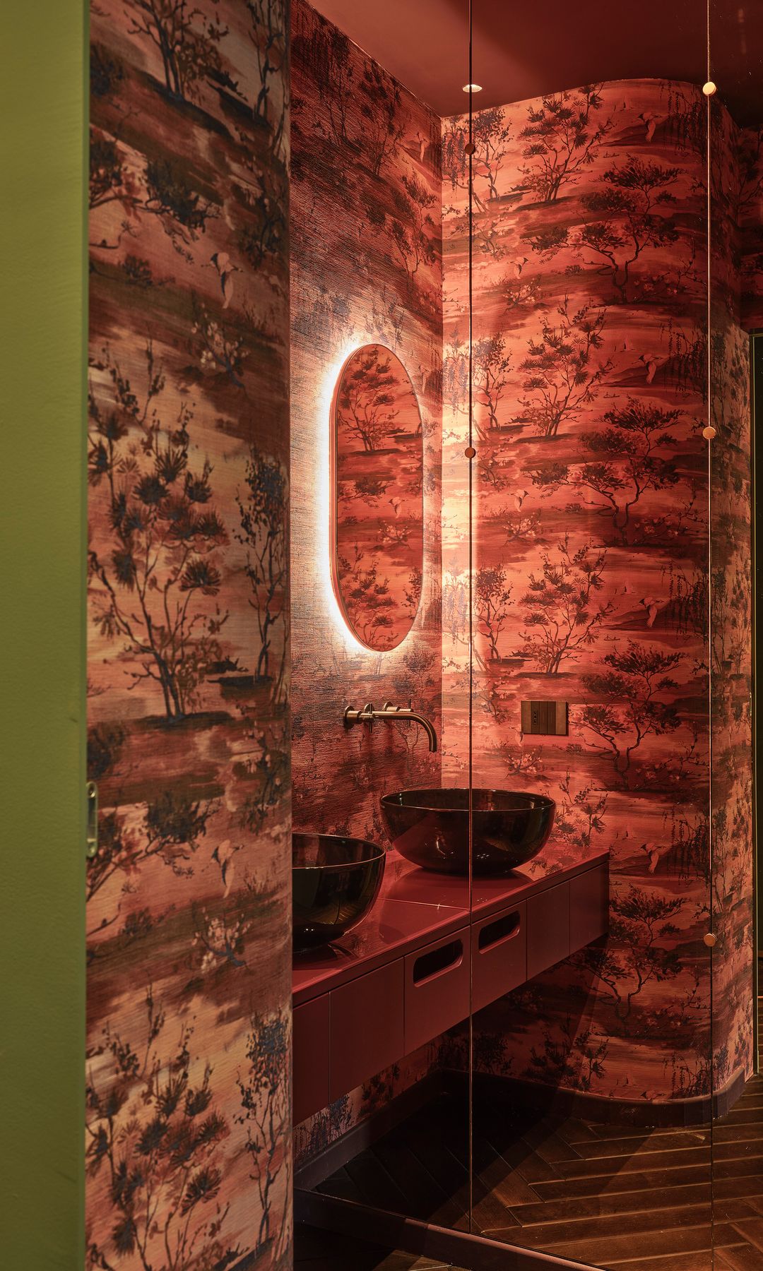 Baño con papel pintado, lavamanos sobre encimera, espejo, suelo de madera 