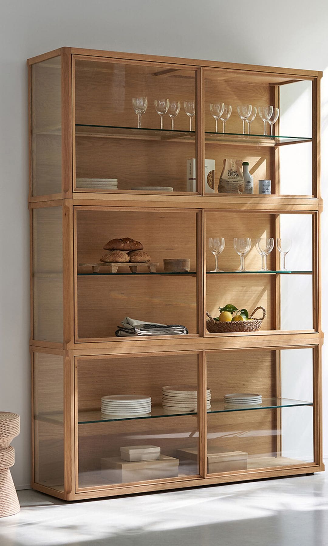 Vitrina de madera XL al lado de un gran ventanal con cortinas blancas, copas y platos en su interior