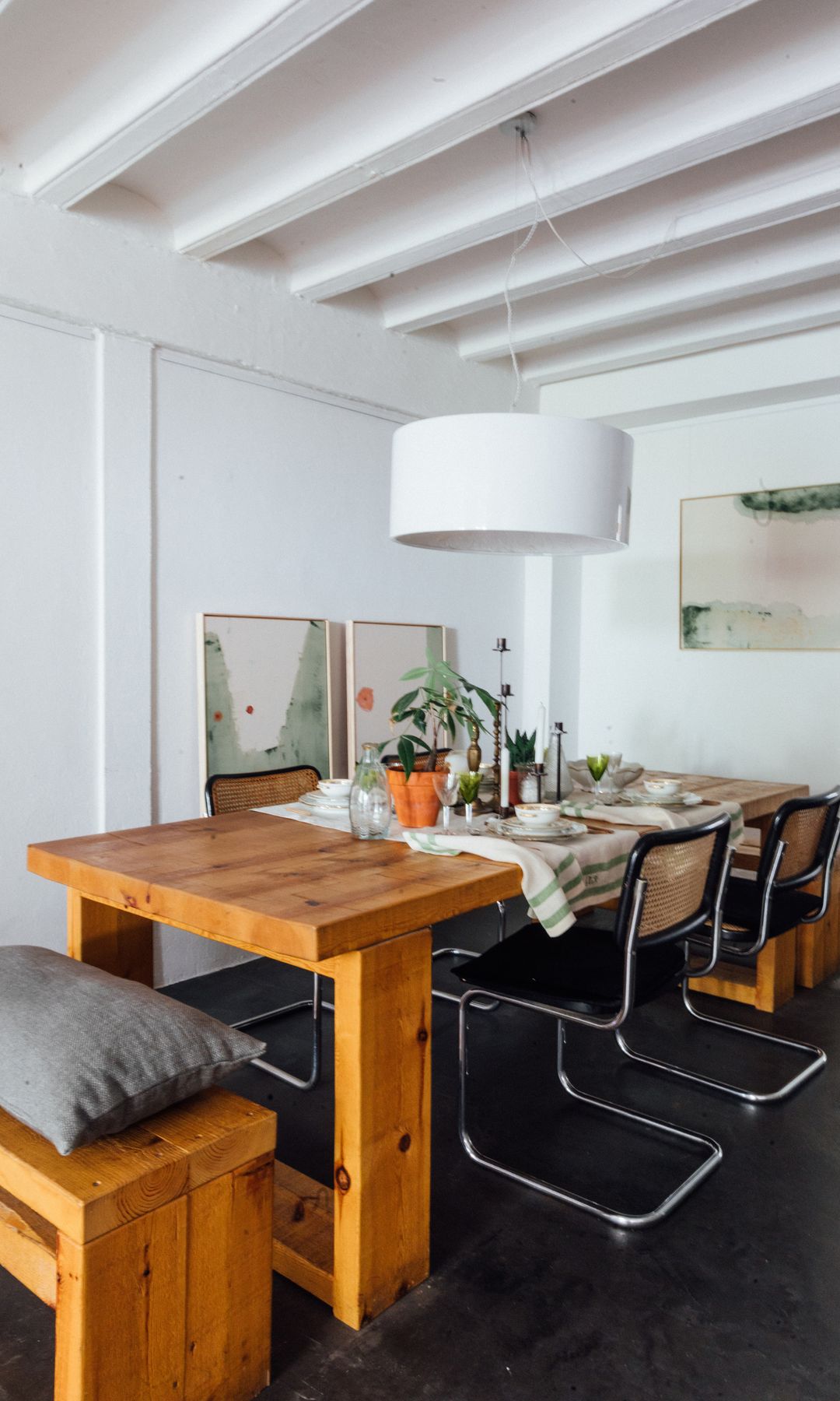 Comedor con sillas Cesca negras, suelo negro, lámpara de techo, banco, mesa de madera, cuadros en las paredes, bovedilla en el techo 