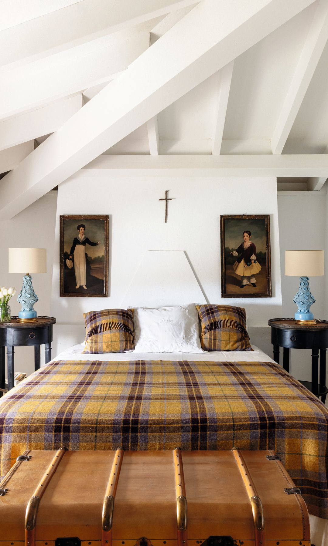 Habitación con cama, baúl antiguo, y cuadros de mujeres en la pared.