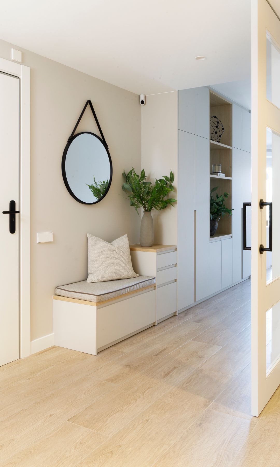 Recibidor comunicado con el salón por puerta corredera de cristal y cuarterones blancos, banco con almacenaje inferior, espejo redondo, armario, mueble con cajones