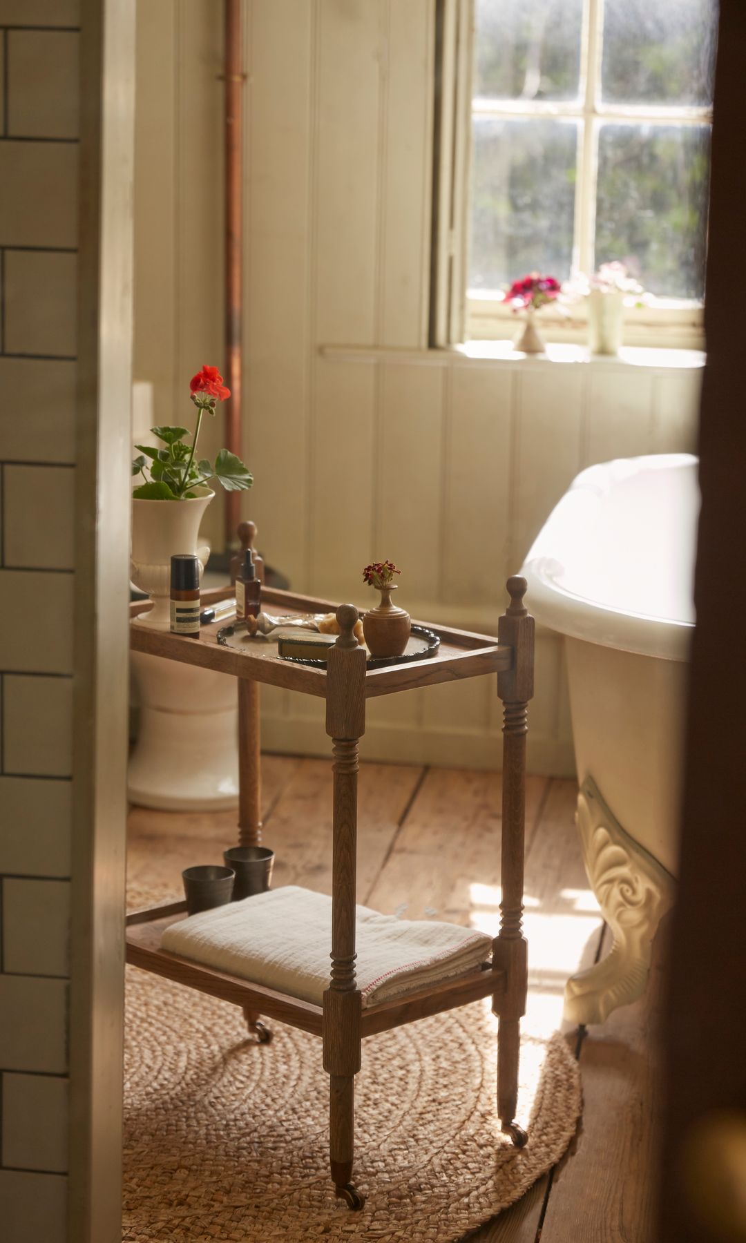 Baño con bañera exenta, carrito auxiliar de madera, alfombra, maceta con flores