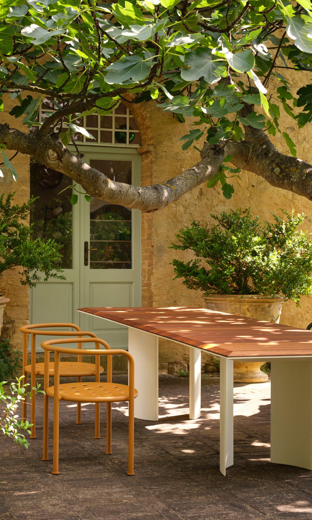 Comedor de verano con mesa de madera anaranjada, árbol gigante y sillas de hierro naranja