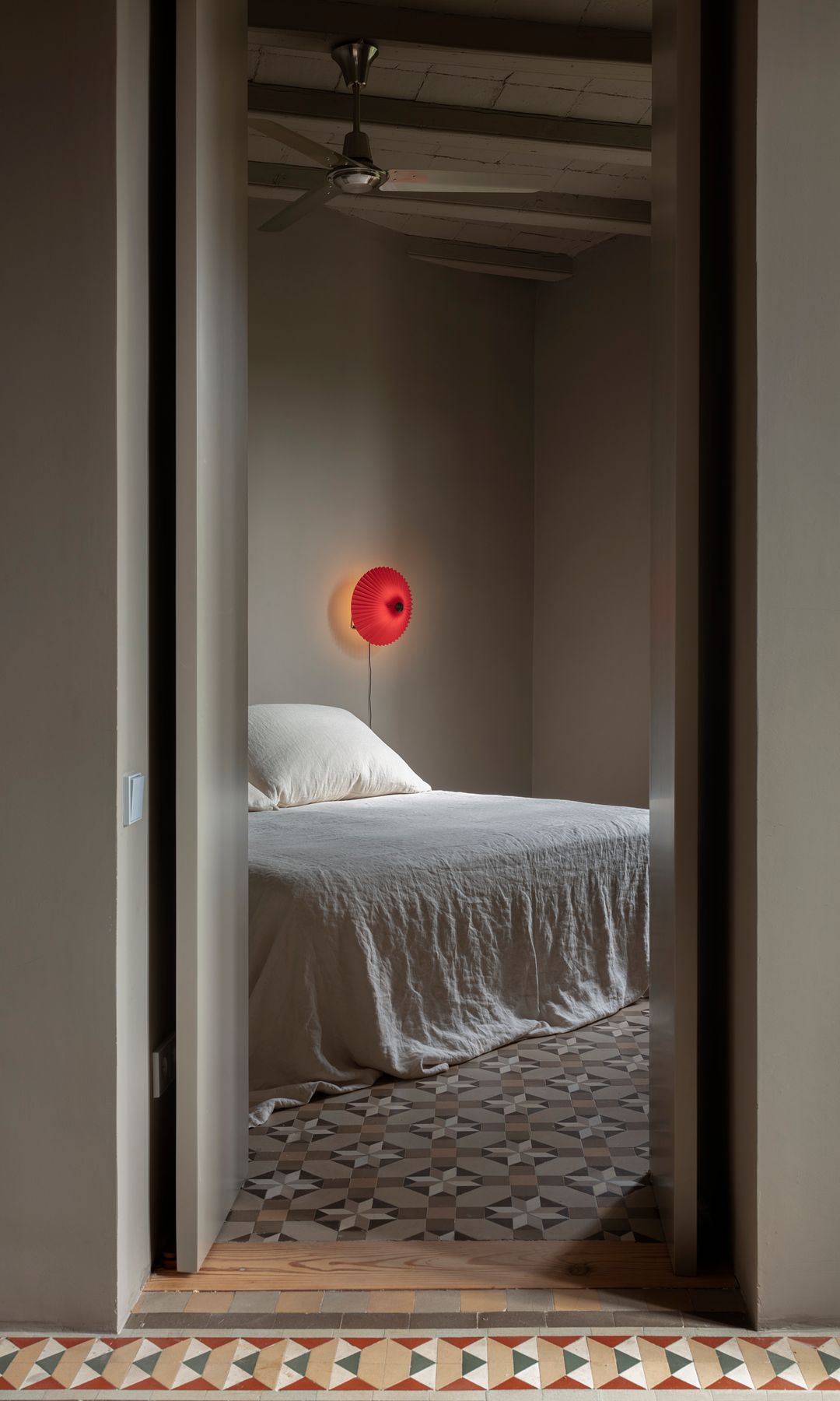 Dormitorio con suelo hidráulico, vigas, ventilador de techo, aplique de pared rojo