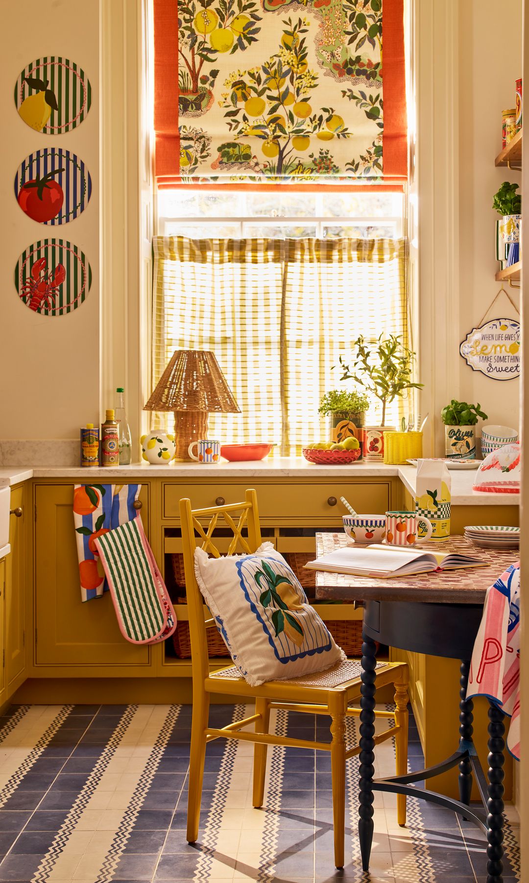 Cocina de color amarillo, con ventana, zona de comedor, estor en la ventana, cortinillas, alfombra, platos en la pared