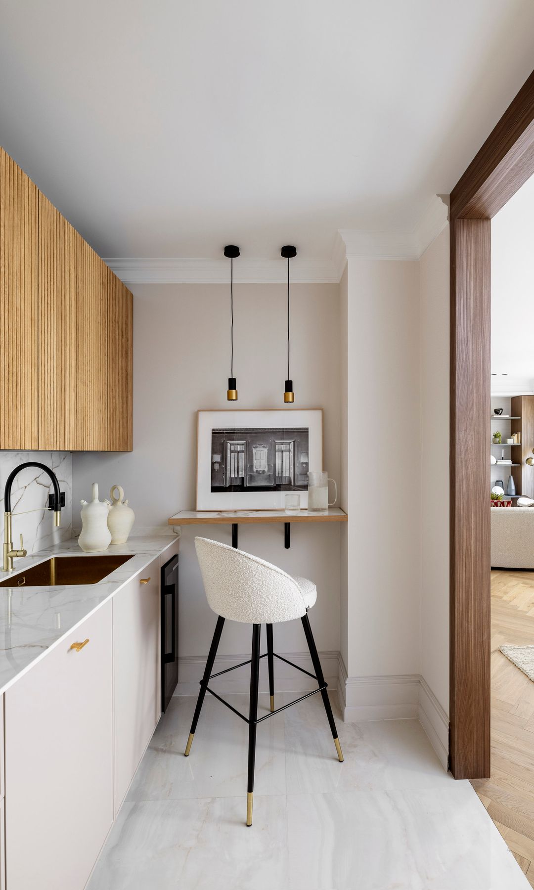 Cocina alargada, con muebles en línea blancos y de madera, zona de office con baldas taburete alto, lámparas de techo