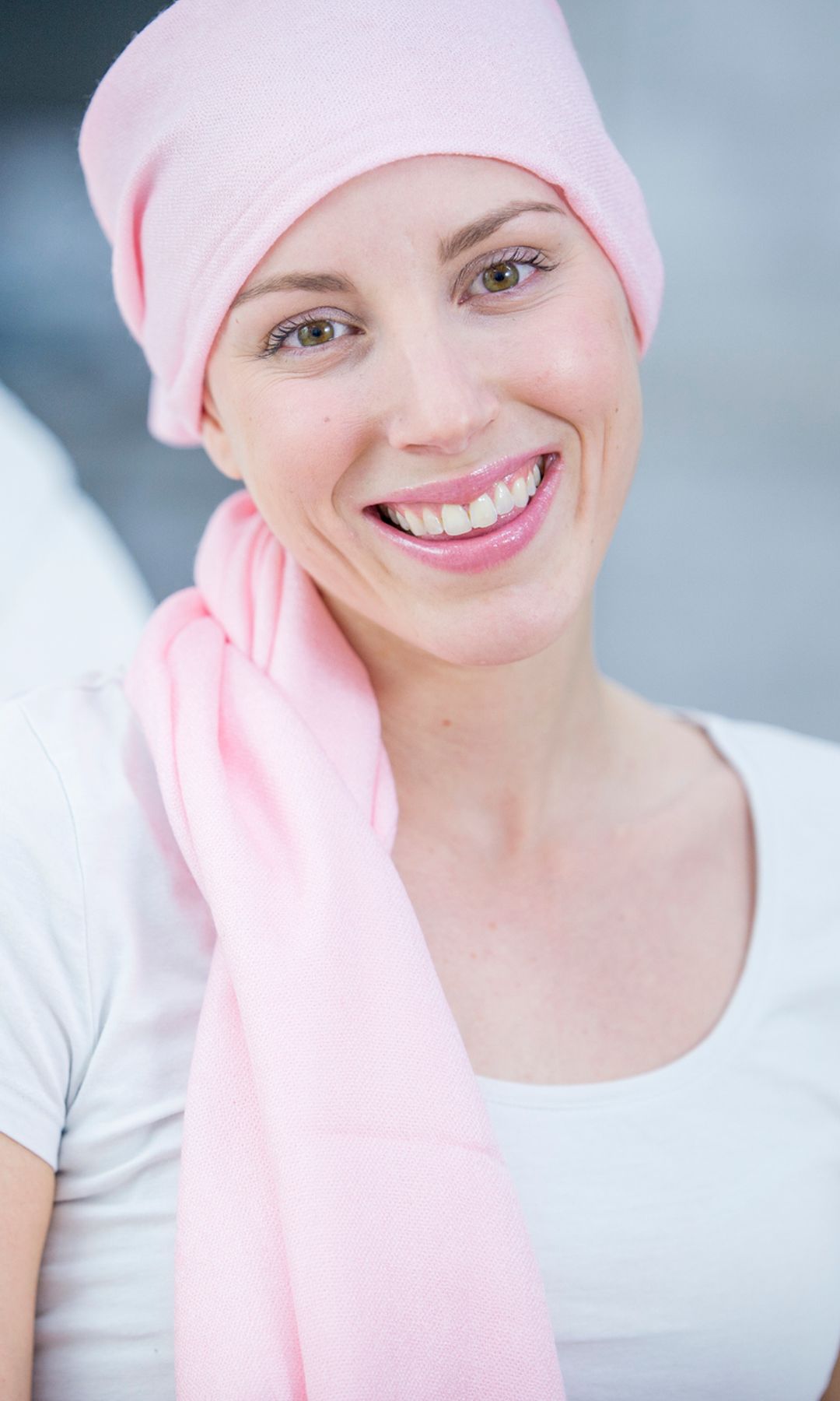Paciente de cáncer de mama con pañuelo rosa sonriendo a cámara