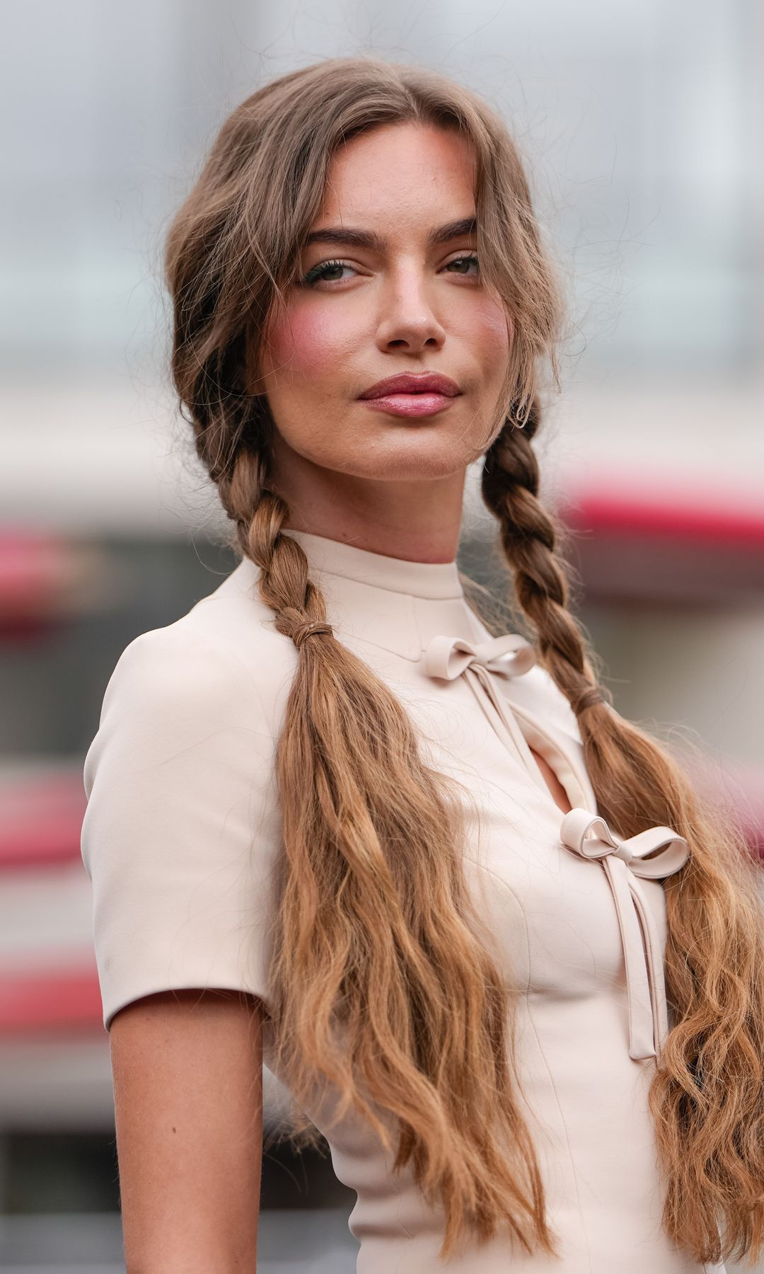 PARIS, FRANCE - JULY 07: A guest wears a cream-colored, short-sleeved top featuring a high collar and a keyhole cutout with a bow detail at the front. Hair is styled in two long braids, outside Georges Hobeika, during Paris Fashion Week - Haute Couture Fall/Winter 2025/2026, on July 07, 2025 in Paris, France 