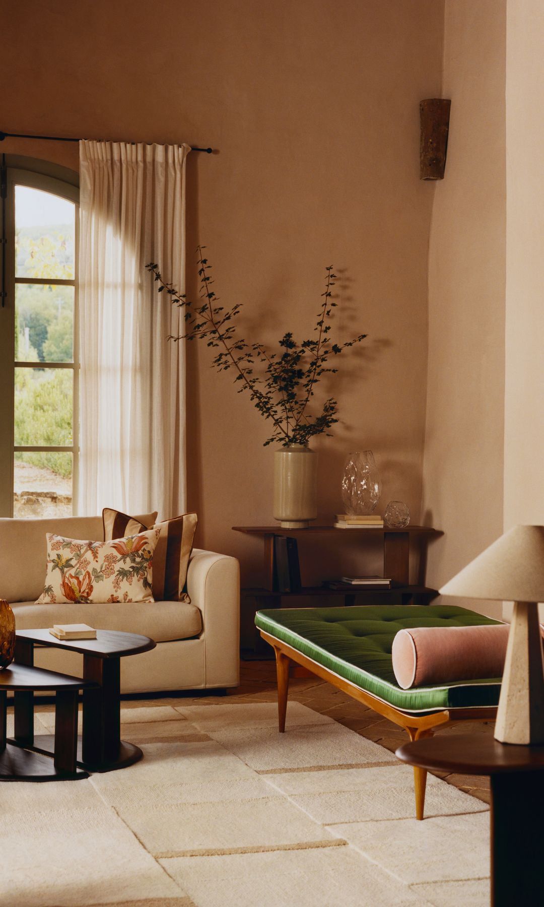 Salón con baldosas, sofá beige, chaise longue verde, cortinas beige, ventana, jarrones, mesa de centro negra, lámpara de sobremesa