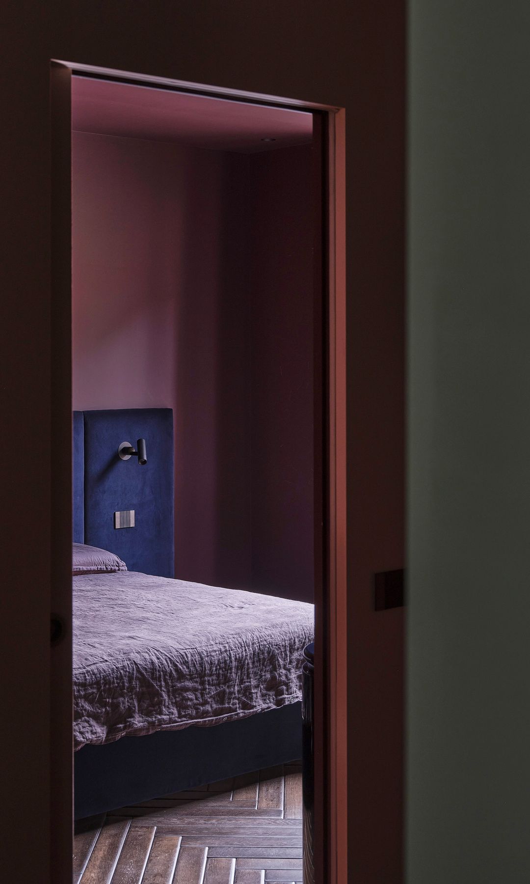 Dormitorio con paredes burdeos, suelo de madera en espiga, cabecero azul 