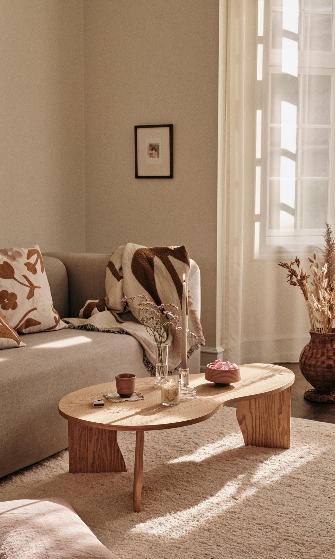 Salón con sofá beige, mesa de centro de madera, jarrón de fibras vegetales en el suelo, cojines, alfombra 