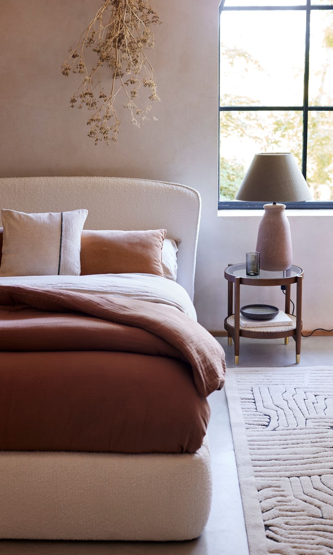 Dormitorio con cama tapizada en color blanco, ropa de cama marrón chocolate, mesita de noche y lámpara de sobremesa 