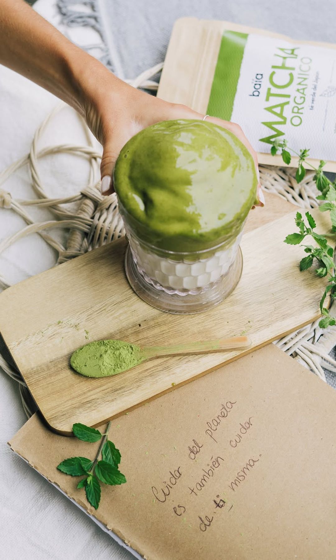 Vaso de matcha latte junto a una bolsa de matcha orgánico y hojas verdes