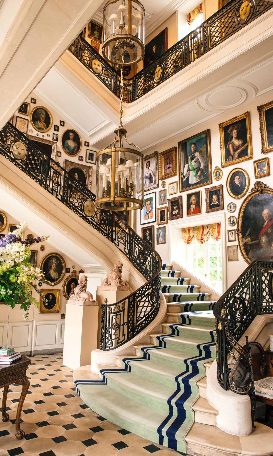 Escalera de mármol con barandillas de hierro forjado, decorada con retratos de personas históricas.