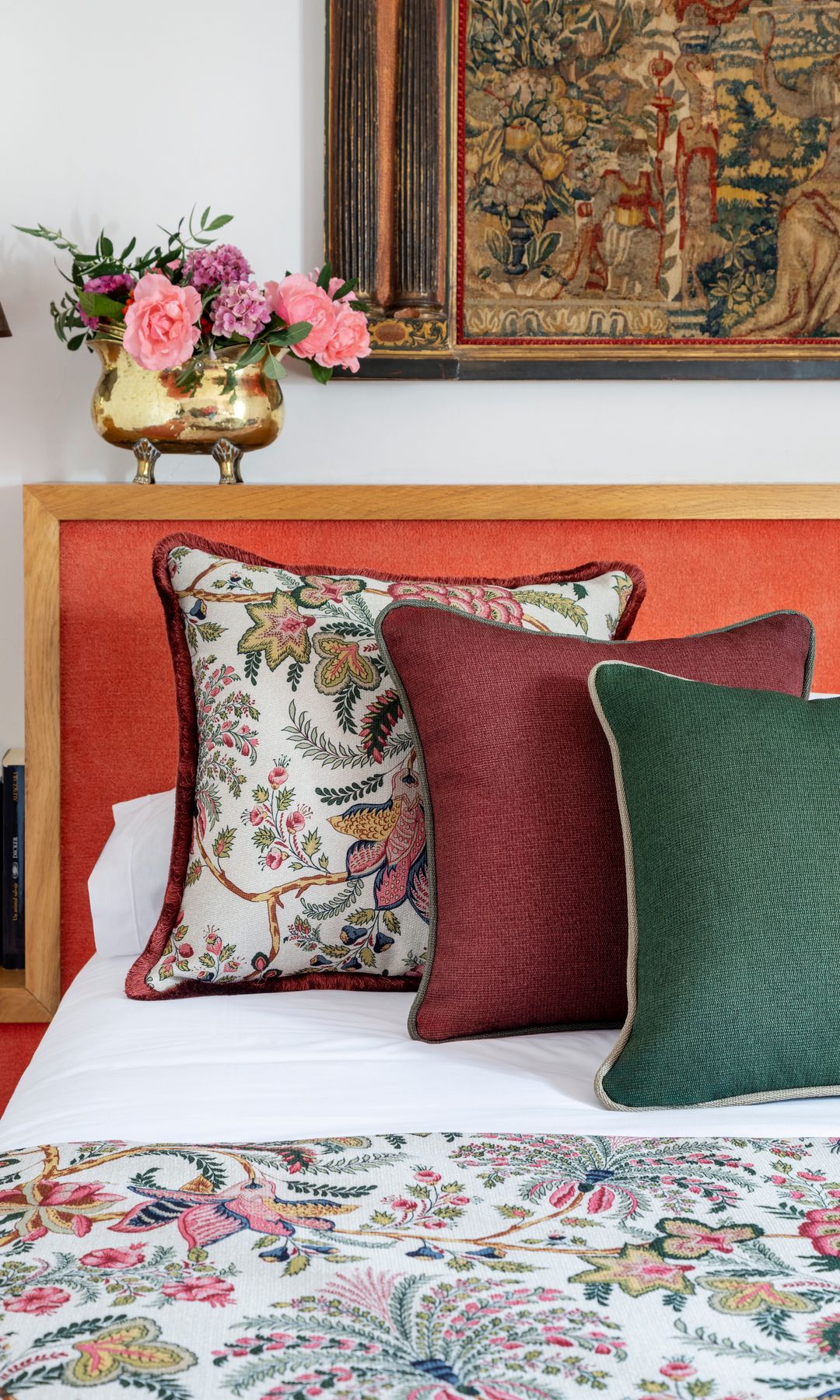 Dormitorio con cabecero tapizado, cojines sobre la cama, arreglo floral, cuadro en la pared del cabecero, funda de flores a juego con uno de los cojines