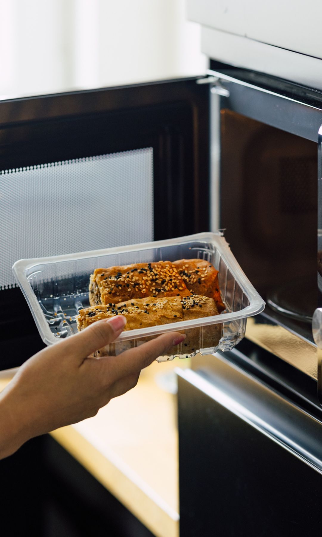 Una mujer metiendo un táper en el microondas