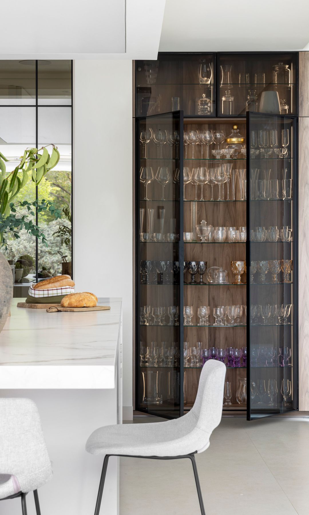 Cocina con vitrina de cristal ahumado negro, con cristalería y vajilla, isla blanca con taburetes altos 