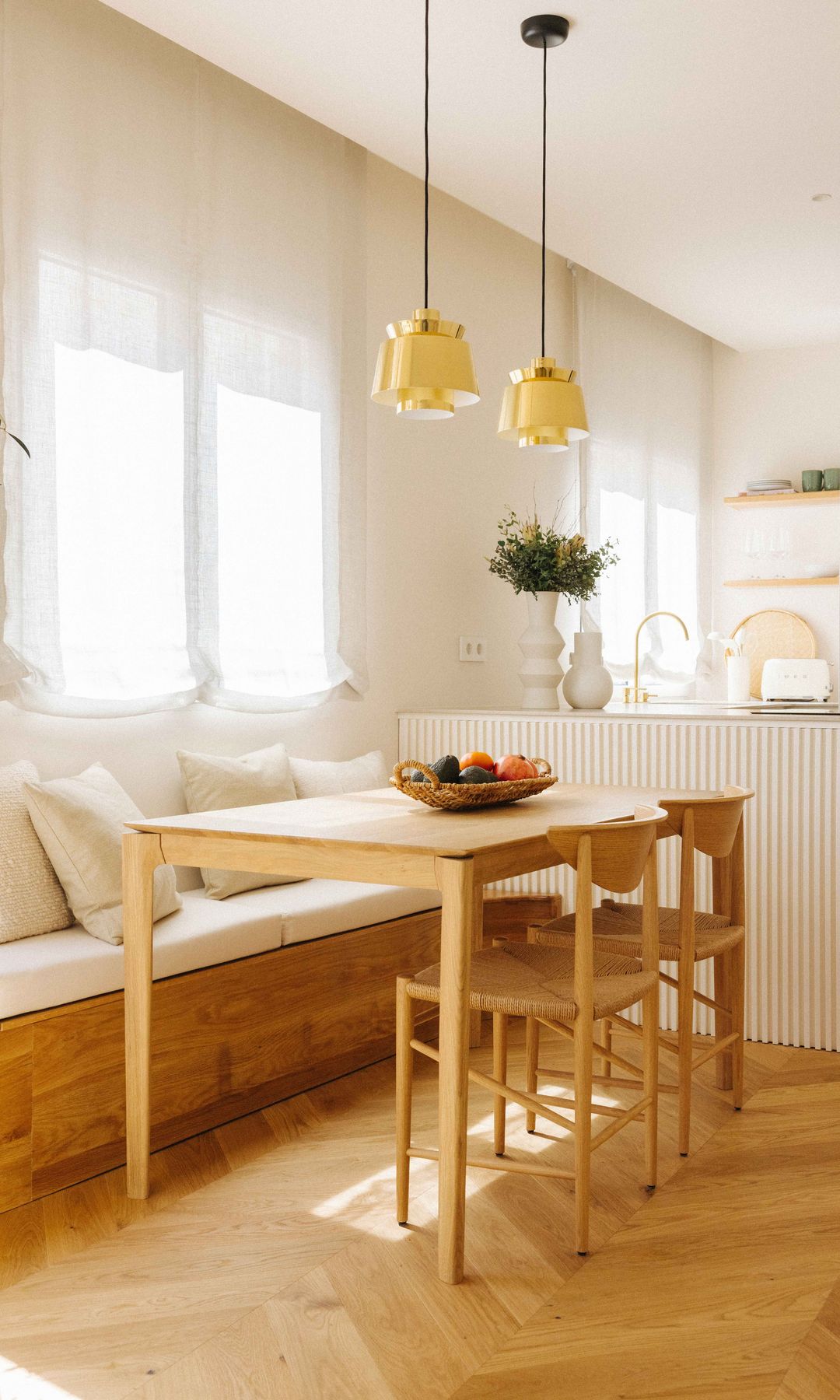 Cocina con comedor con banco de madera, estores, sillas y mesa de madera, lámparas de techo