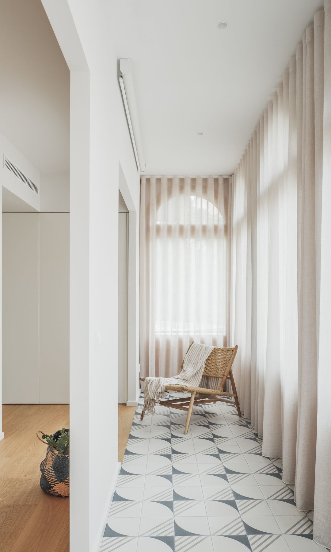 Galería con baldosas hidráulicas, cortinas blancas, sillón de fibras vegetales
