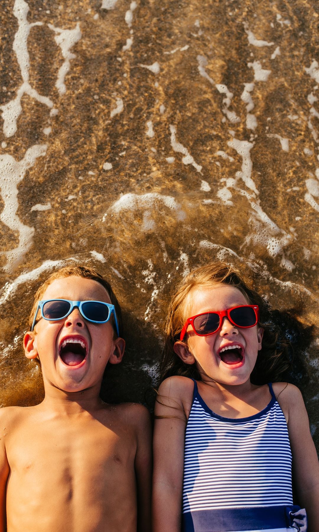 Niños sonríen tumbados en la playa en sus vacaciones de verano