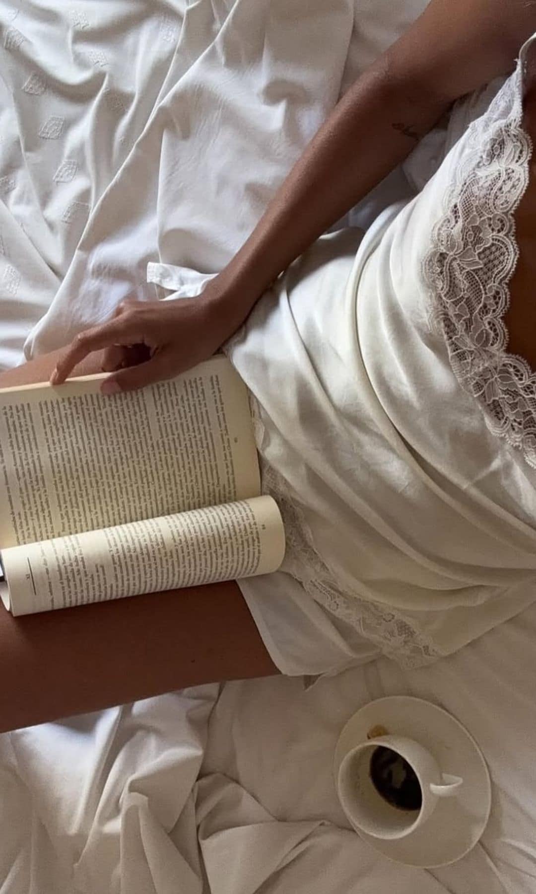 Una chica leyendo en camisón en la cama tomando café