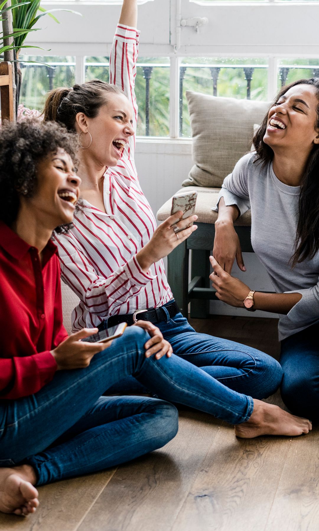 Tres mujeres ríen y se divierten en una sala con ventanas grandes, acto que les da felicidad