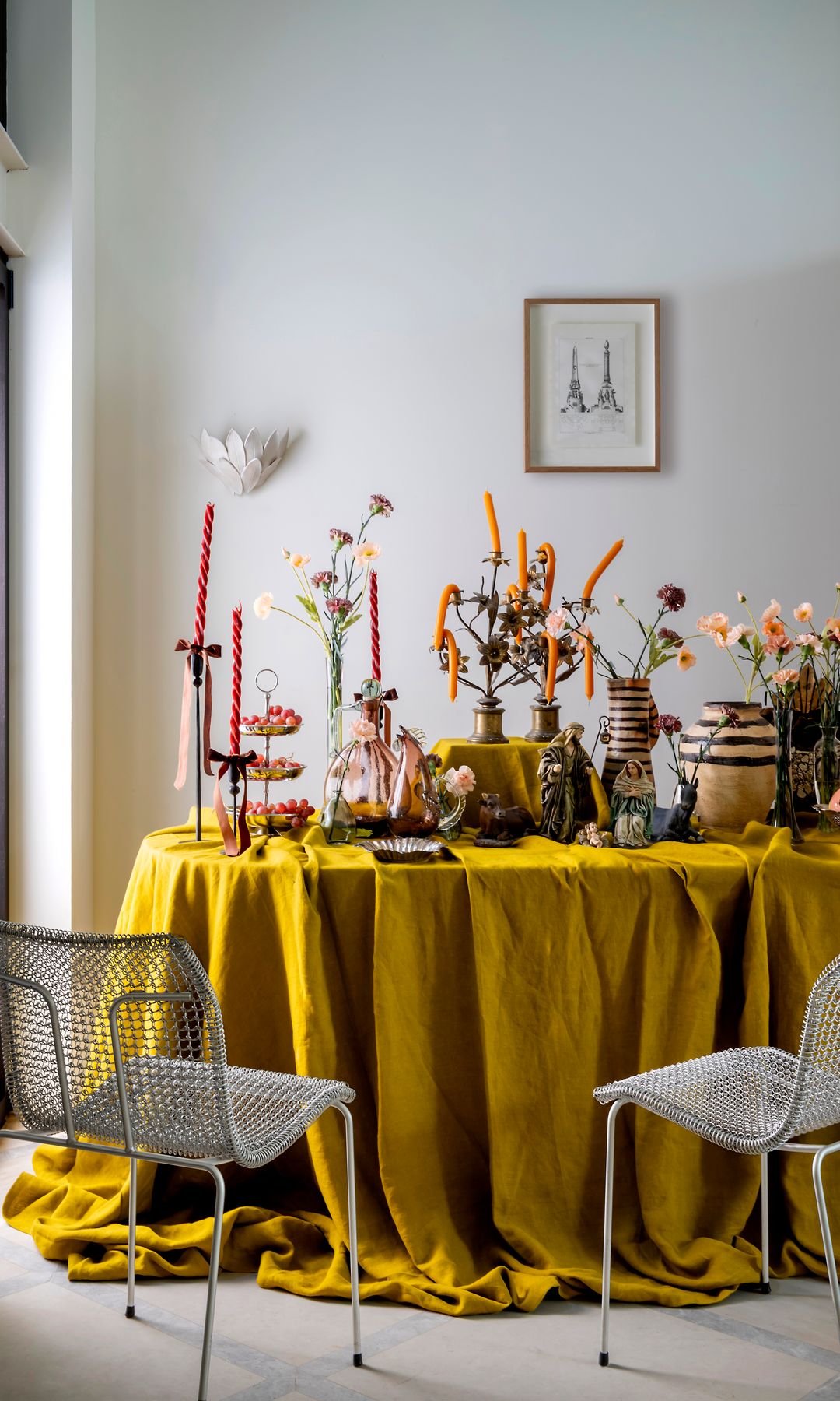 Mesa de navidad con mantel mostaza, centros de mesa, arreglos, velas, vajilla, sillas metálicas sin brazos