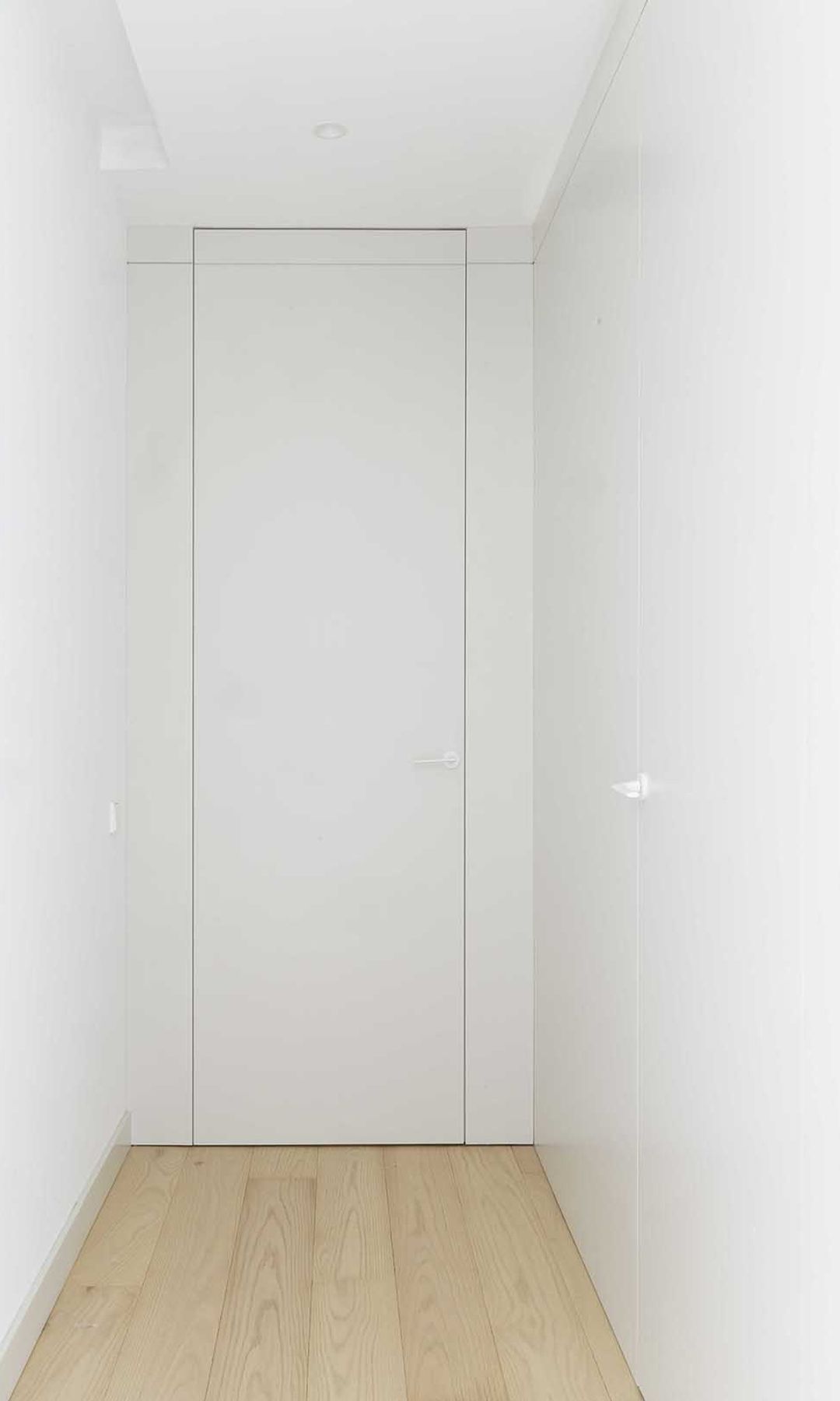 Pasillo blanco con armarios y paredes del mismo color, suelo de madera claro, focos empotrados