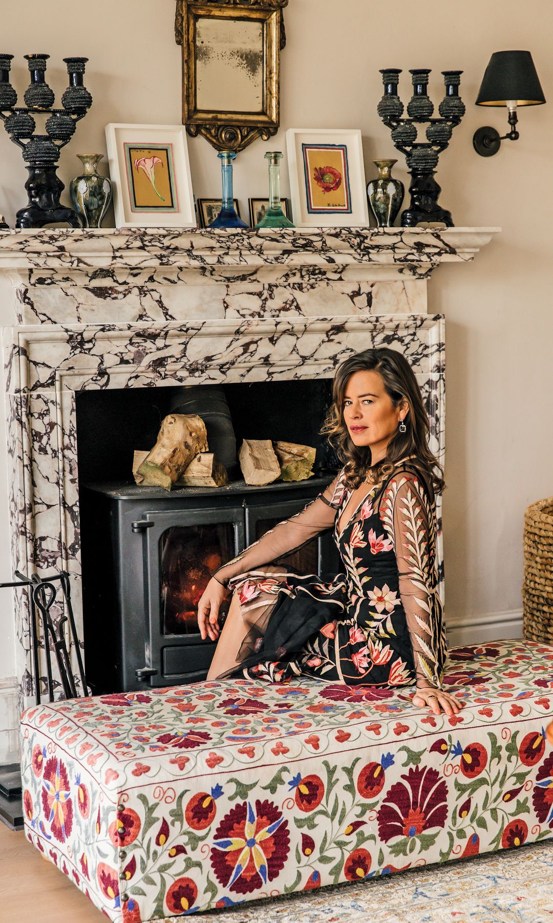Jade Jagger sentada en un banco frente a una chimenea en una sala.