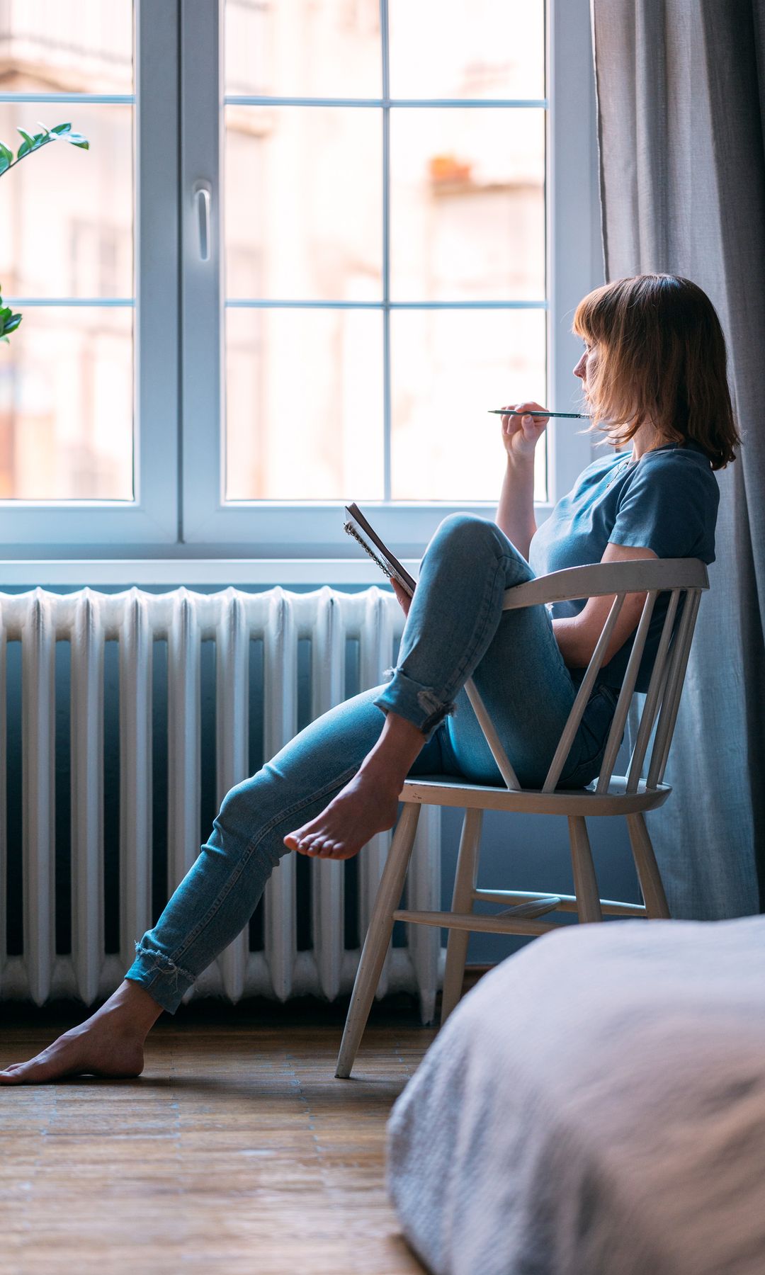 una mujer apuntando datos en su agenda, sentada en una silla y mirando por la ventana